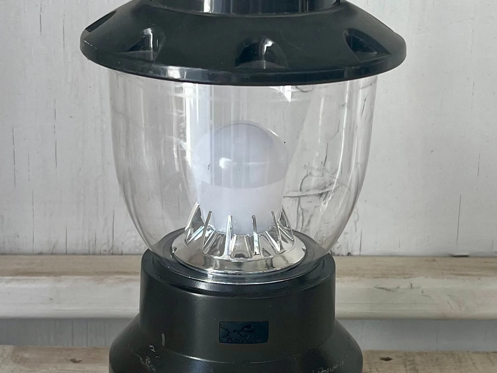 Eine helle LED-Campinglaterne steht eingeschaltet auf einer Fläche und dient als netzunabhängige Lichtquelle.
