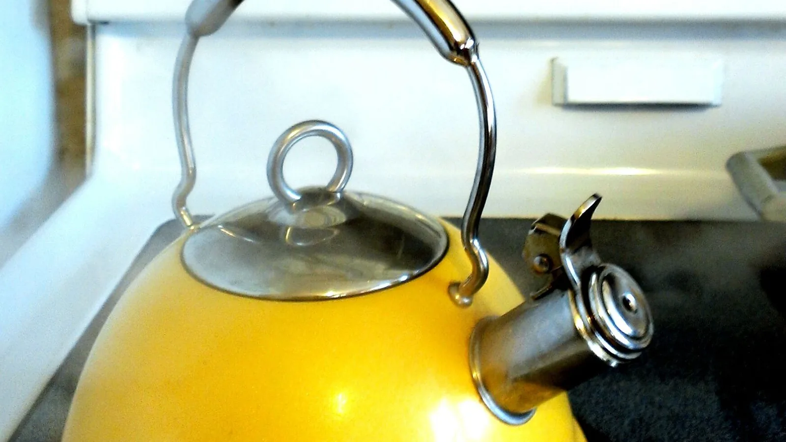 Ein gelber Wasserkessel mit kochendem Wasser steht auf einer Herdplatte.