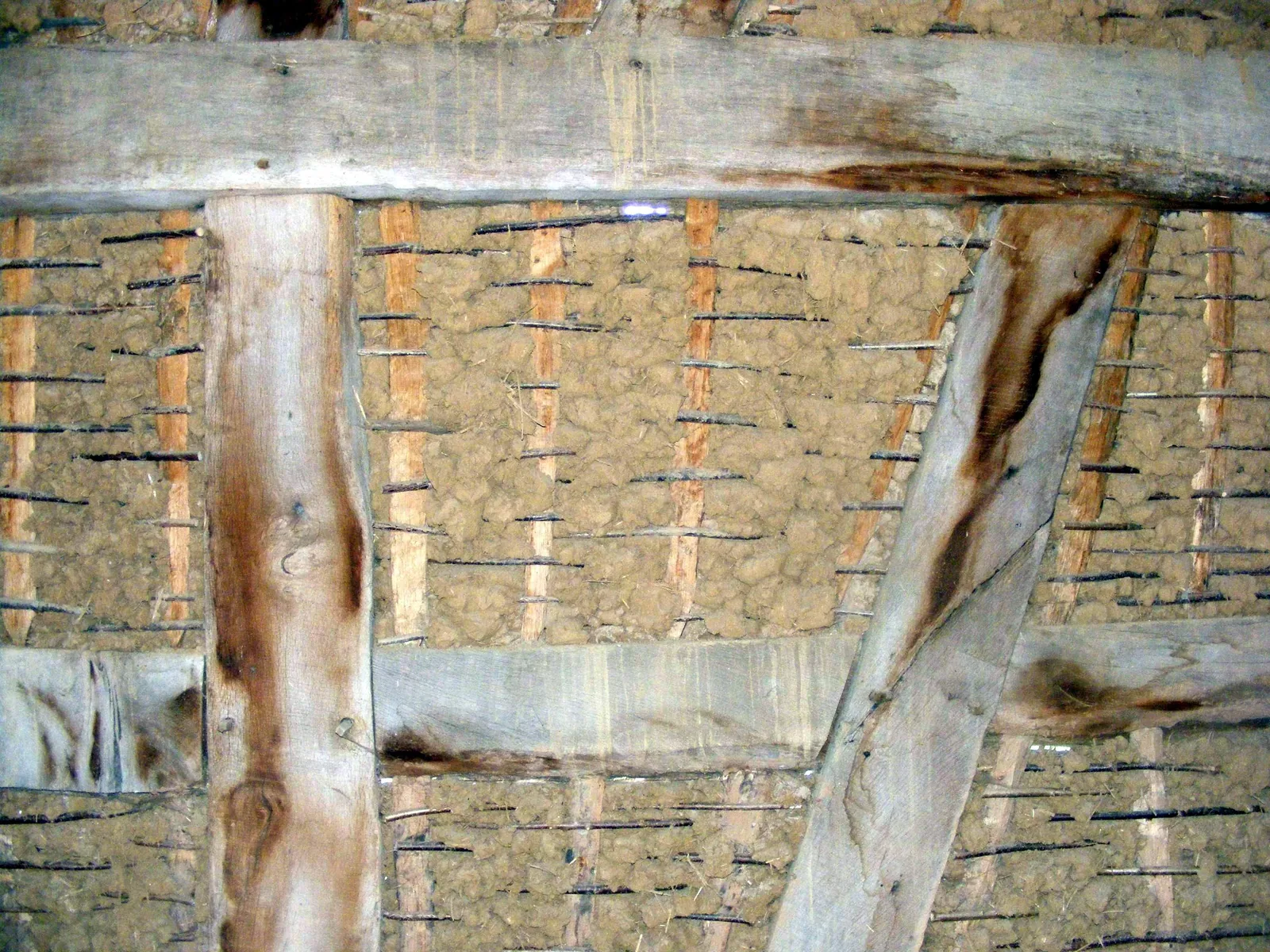 Innenansicht einer Fachwerkwand: Zwischen den Holzbalken stecken senkrechte Staken, umflochten mit dünnen Hölzern und mit Lehm gefüllt.