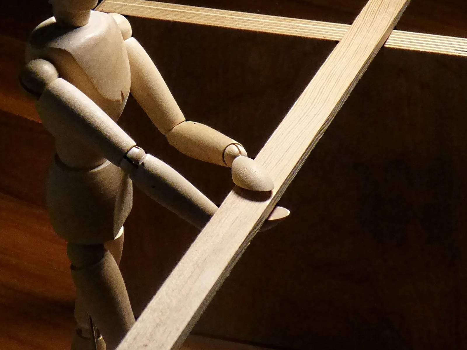 Ein einfacher zweiseitiger Hebel aus Holz balanciert ein Messinggewicht gegen eine Holzfigur über einem festen Drehpunkt.