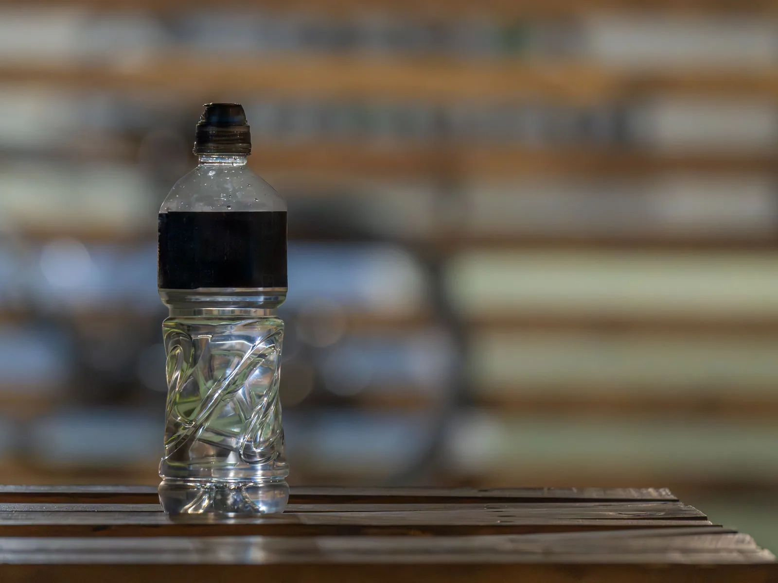 Eine transparente Kunststoffflasche mit Wasser steht auf einer Ablage vor unscharfem Hintergrund.
