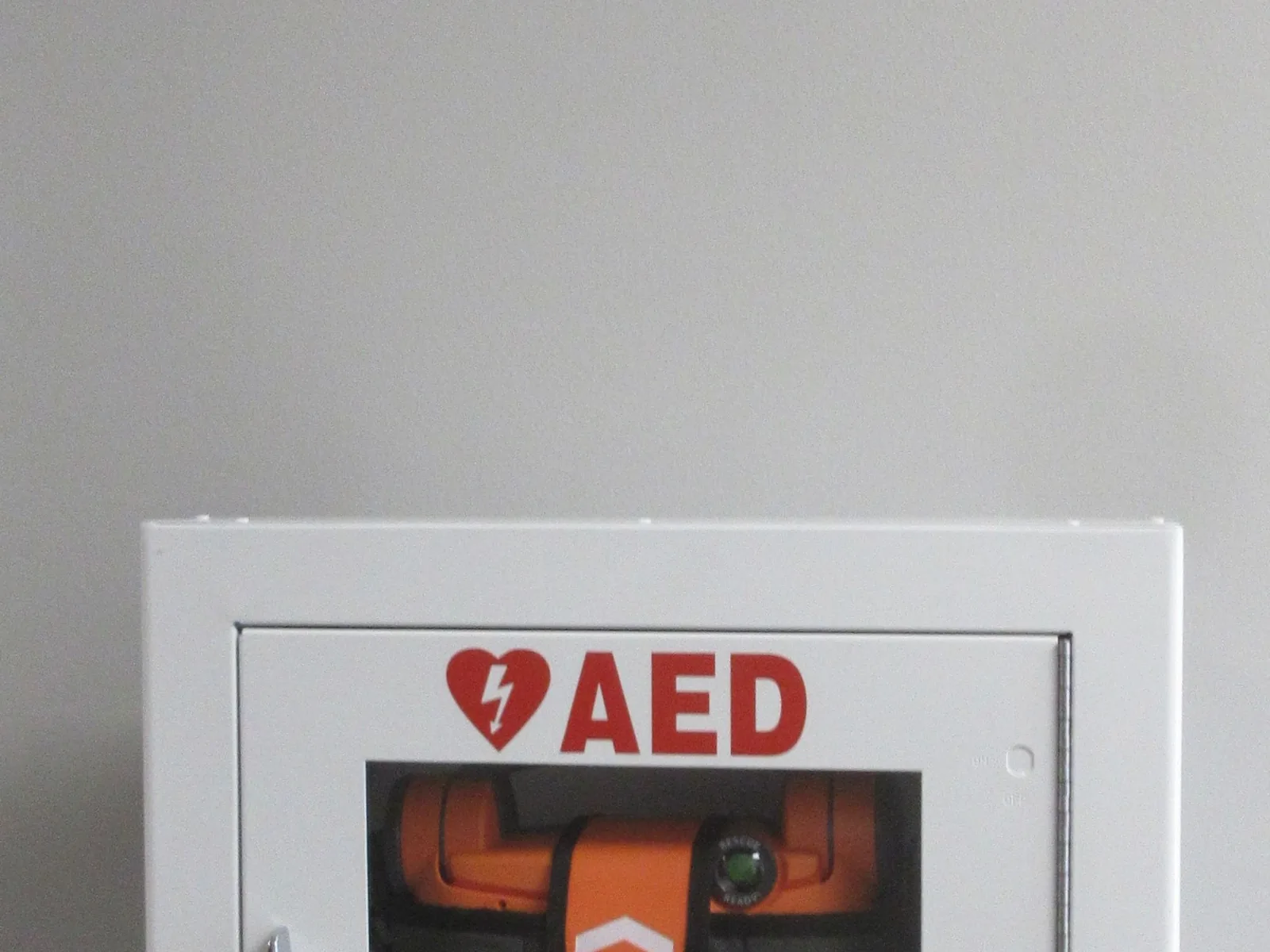 Ein automatisierter externer Defibrillator befindet sich in einem Wandkasten; darüber weist ein AED-Schild auf den Standort hin.