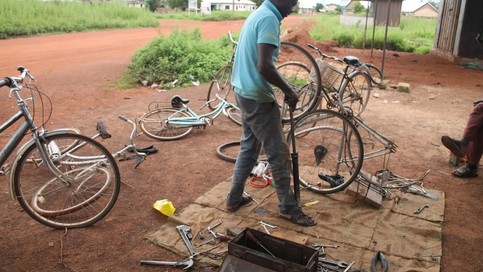 Eine Person repariert ein Alltagsfahrrad auf einer Arbeitsfläche; mehrere Fahrräder und Handwerkzeuge liegen daneben.
