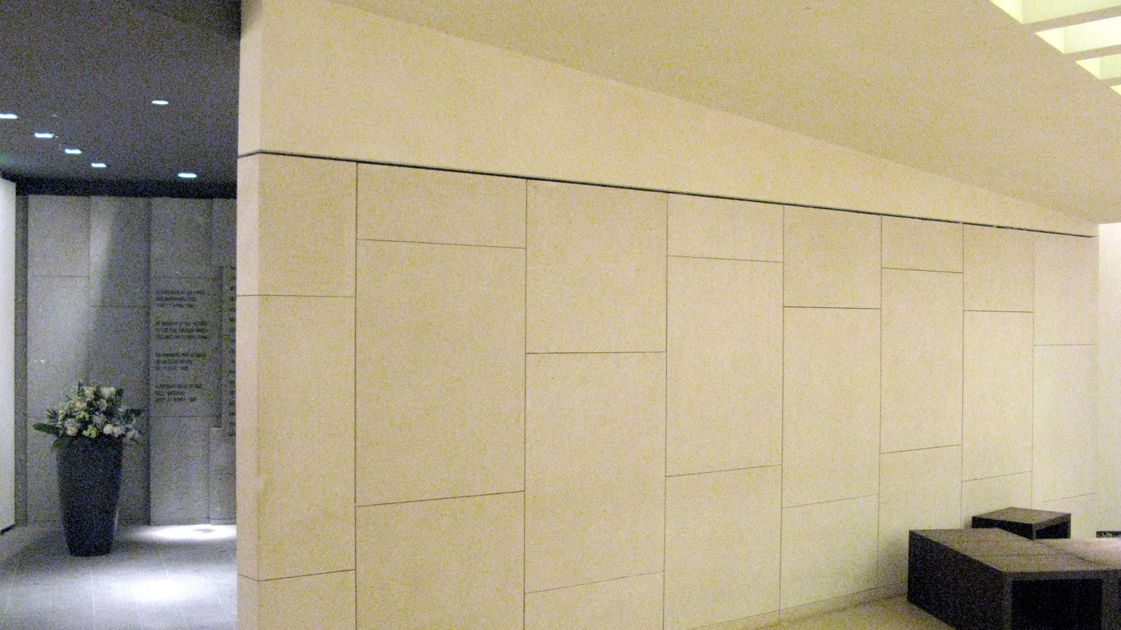 Gedenkraum im Flughafen Düsseldorf mit heller Steinwand, Sitzbank und einer Nische zur Erinnerung an die Brandkatastrophe von 1996.