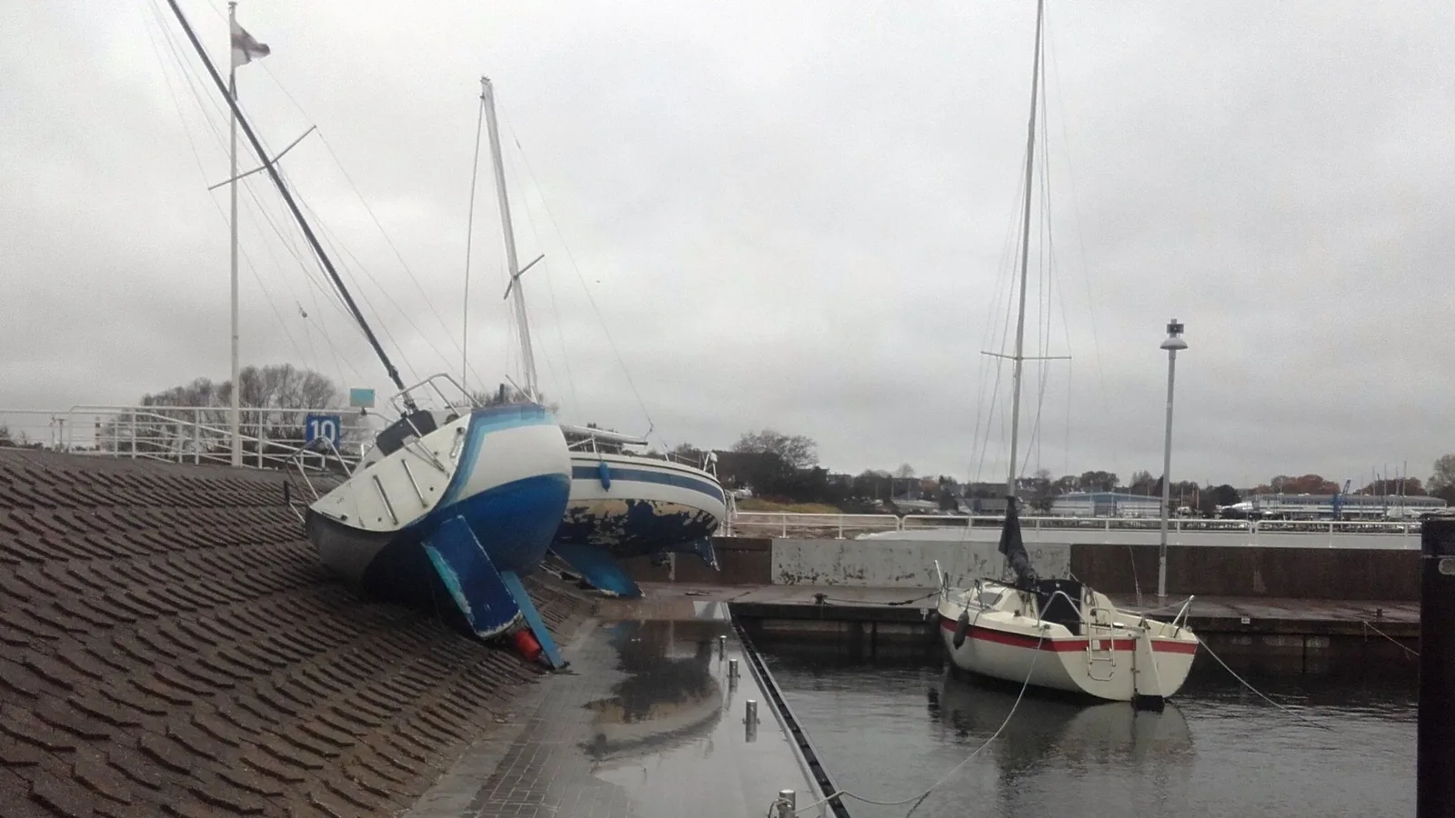 Zwei Segelyachten liegen schräg auf einer gepflasterten Uferböschung im Hafen, eine dritte schwimmt noch am Steg; der Himmel ist grau.