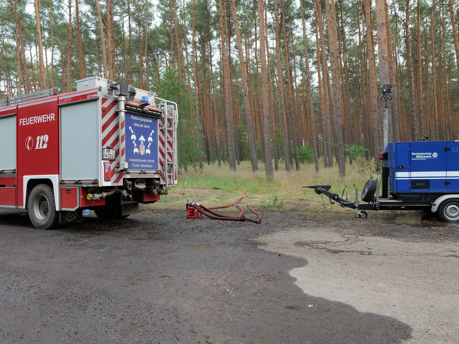 Ein Tanklöschfahrzeug der Feuerwehr steht an einer Löschwasserentnahmestelle am Rand eines Kiefernwalds, daneben ein Pumpenanhänger des THW und Schläuche.