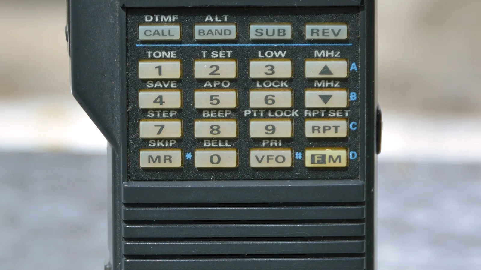 Ein tragbares Amateurfunk-Handgerät mit Antenne und Bedienelementen liegt auf einer neutralen Oberfläche.