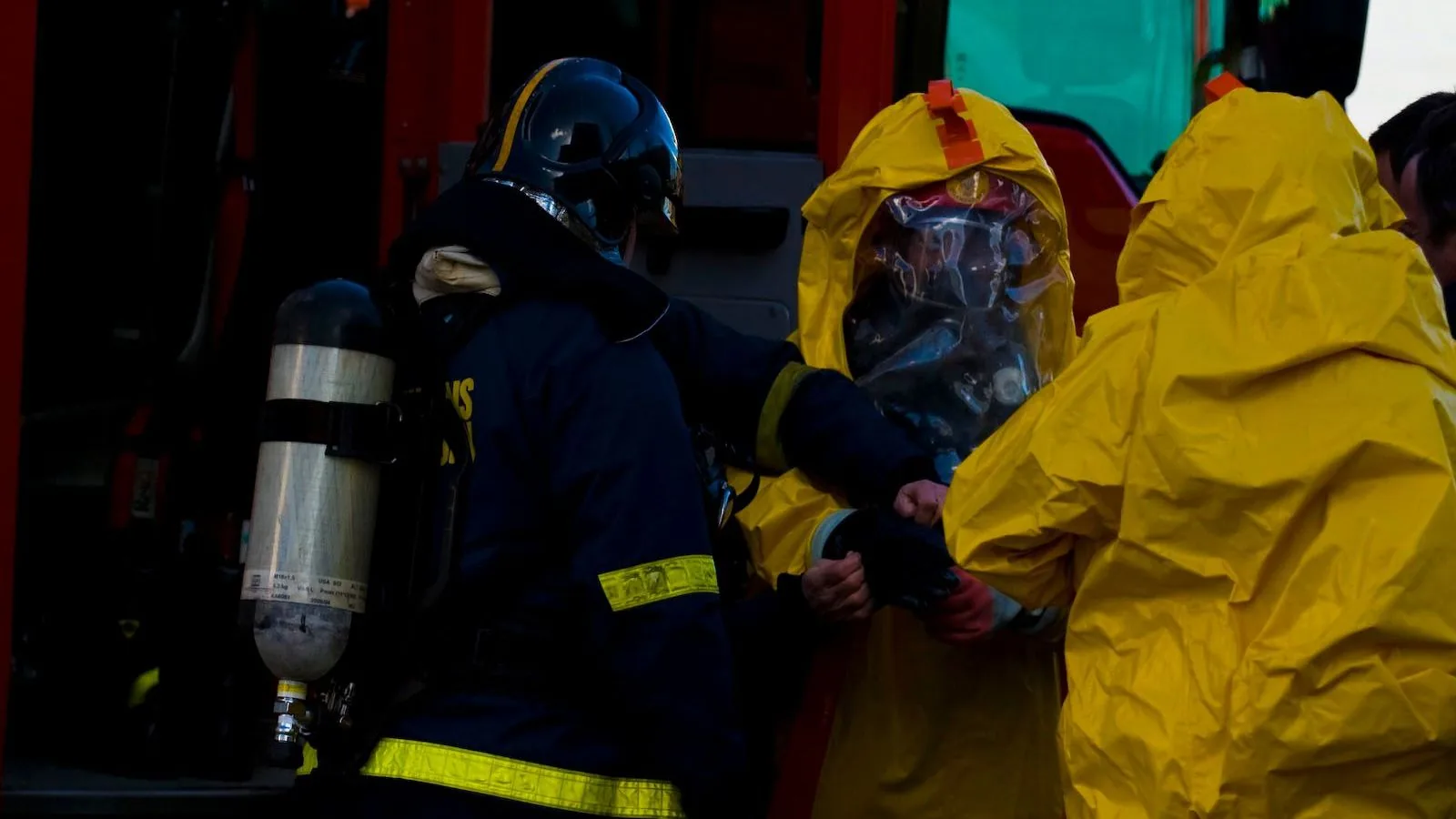 Feuerwehrleute legen vor einem Einsatz geschlossene Gefahrstoffschutzanzüge an.