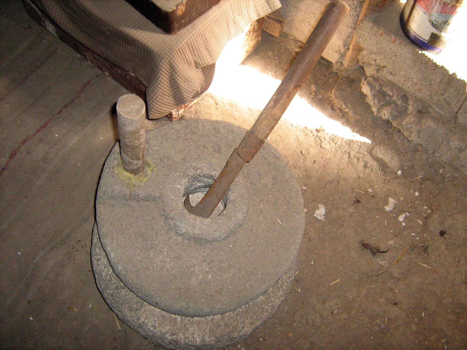 Eine traditionelle Handmühle aus zwei übereinanderliegenden Mahlsteinen wird mit einem seitlichen Griff gedreht.