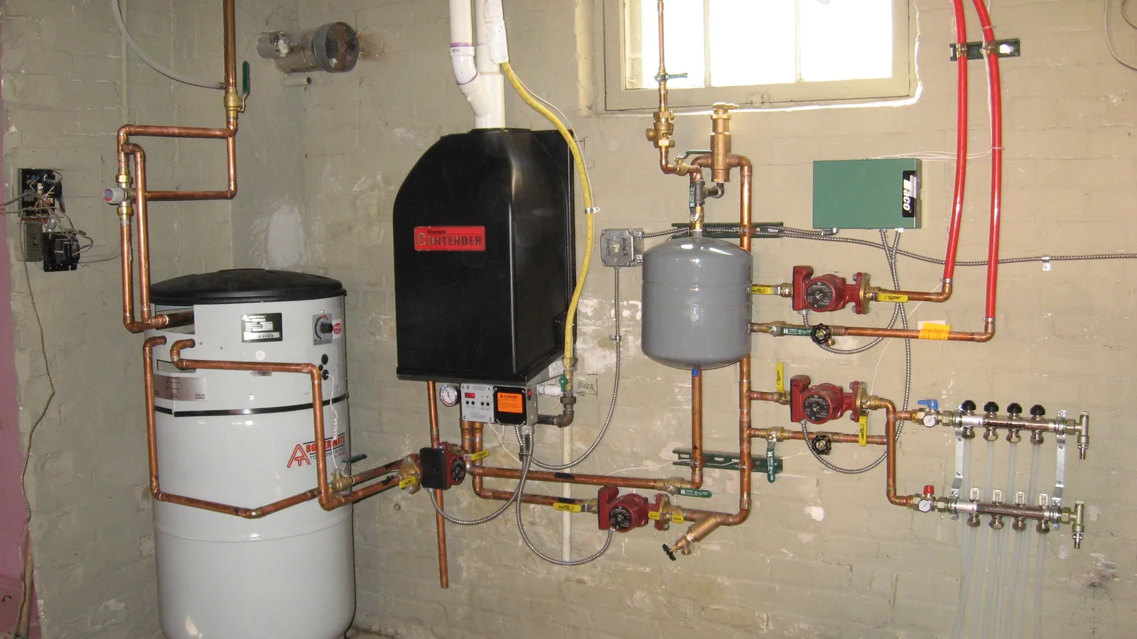 Eine moderne Heizungsanlage mit Brennwertkessel, Warmwasserspeicher, Rohrleitungen und Umwälztechnik ist in einem Technikraum installiert.