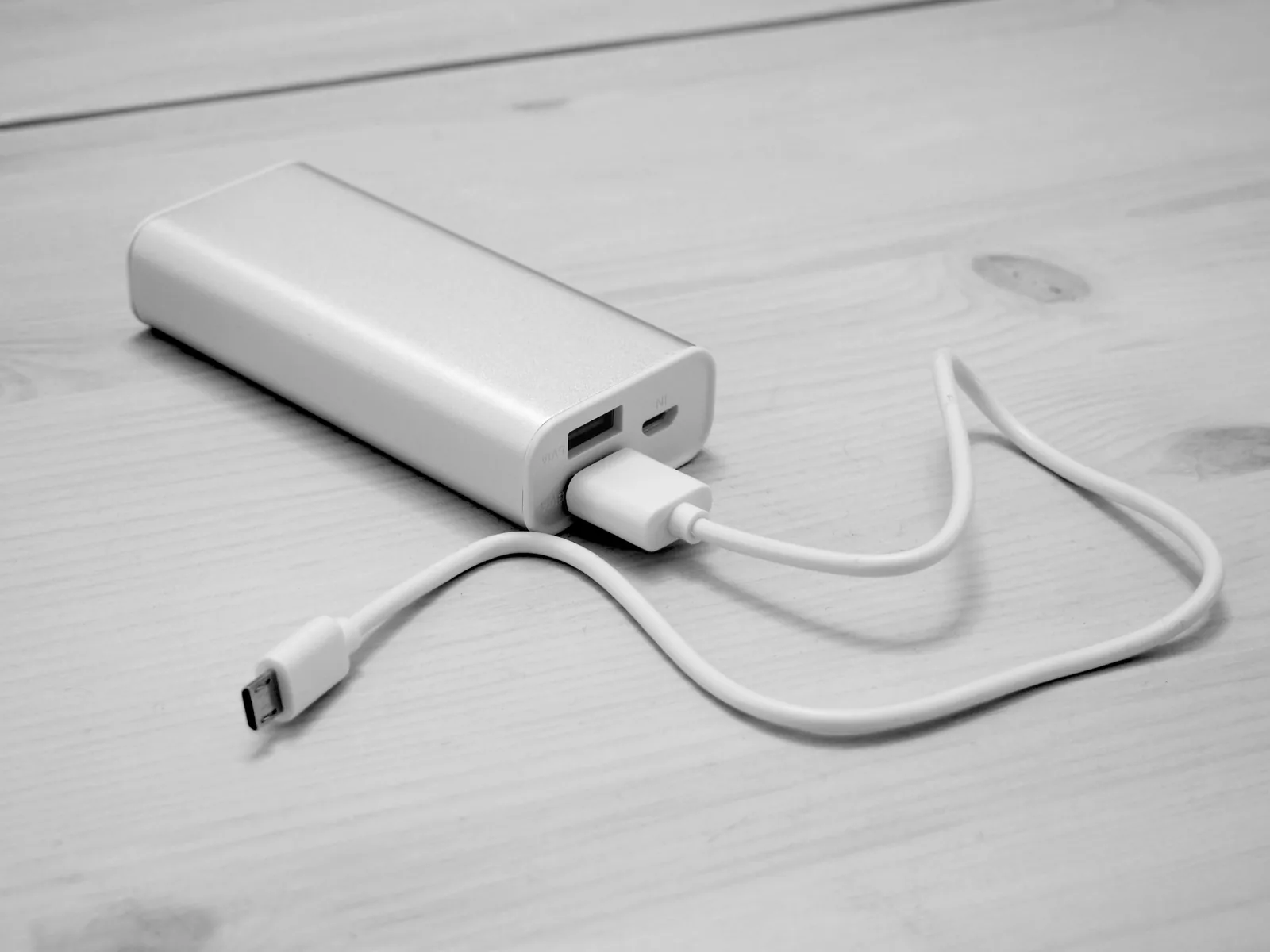 Eine weiße Powerbank liegt auf einem Holztisch, ein USB-Kabel ist eingesteckt.