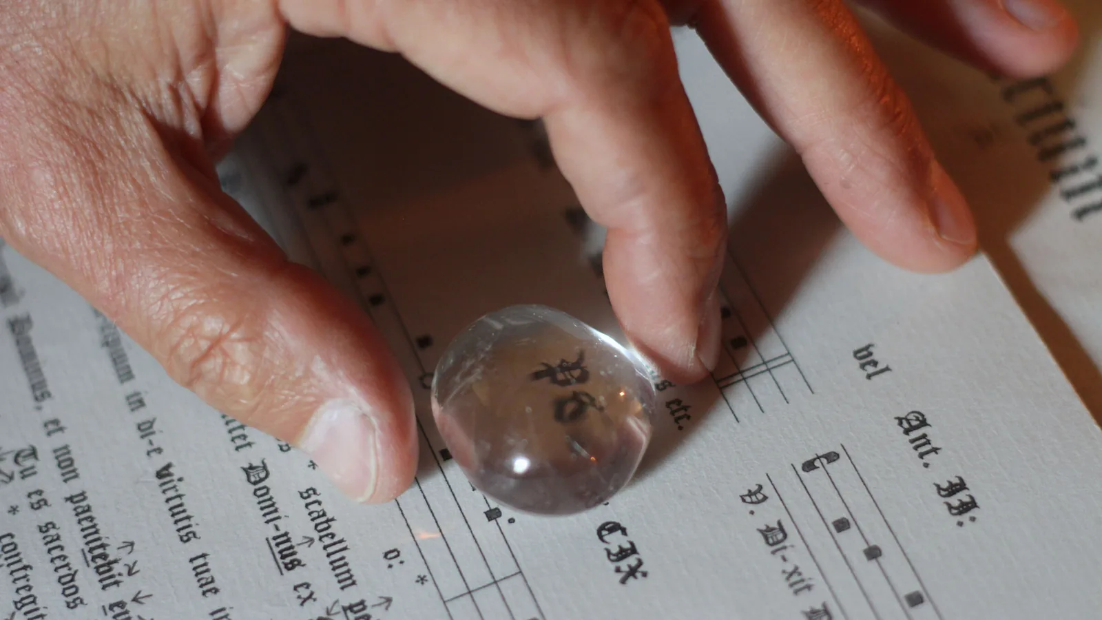Eine Hand legt einen halbkugeligen Lesestein aus klarem Glas auf eine alte, gedruckte Buchseite; die Buchstaben darunter erscheinen deutlich größer.