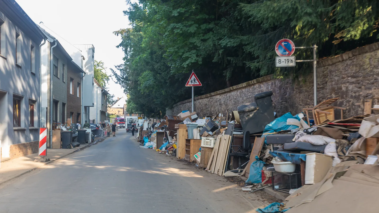 Eine Dorfstraße in Flamersheim: Am Straßenrand stapeln sich nach dem Hochwasser durchnässte Möbel, Teppiche, Bretter und Hausrat.