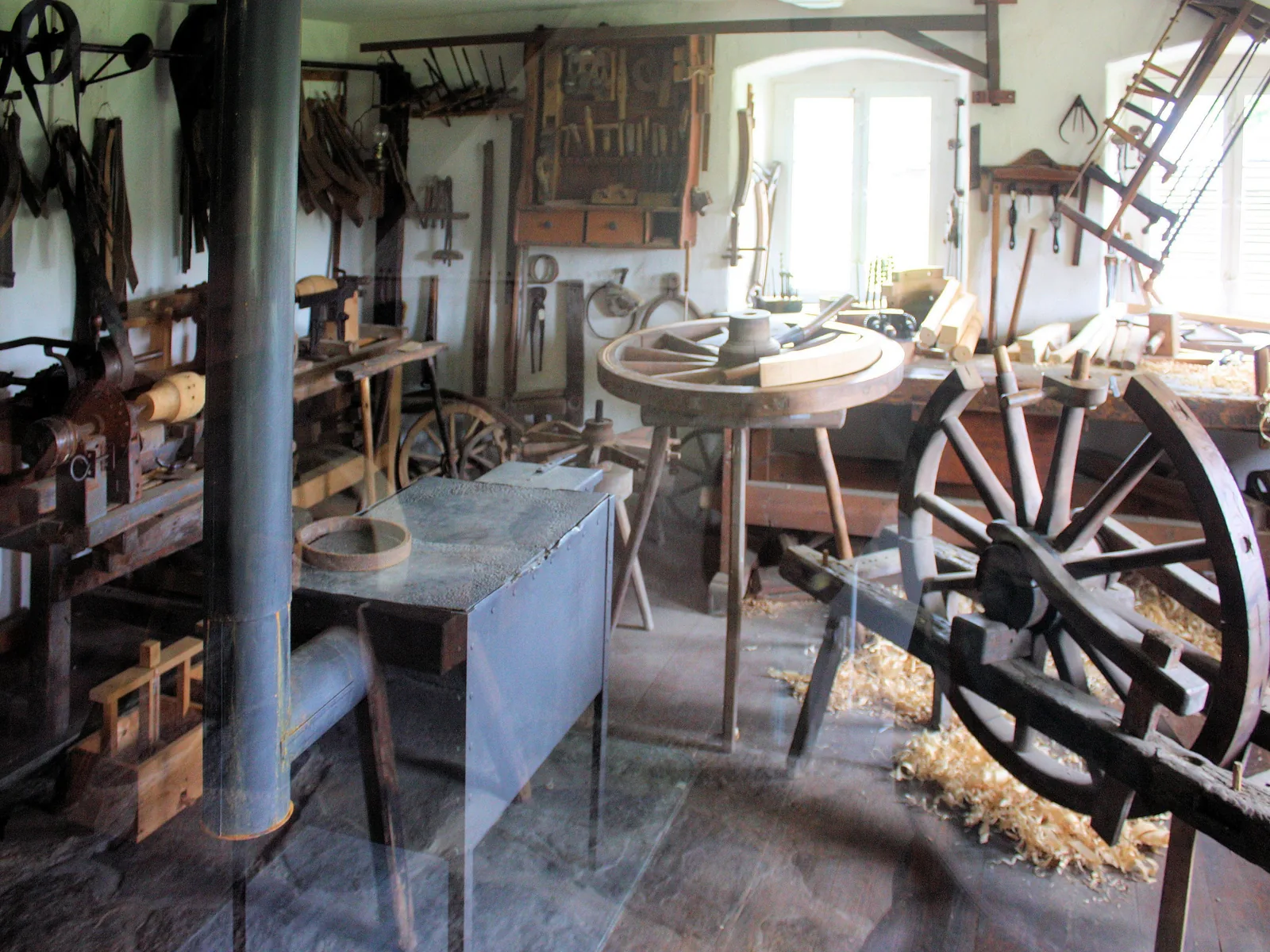 Blick in eine historische Stellmacherwerkstatt: Werkbänke, Werkzeug an den Wänden und im Vordergrund ein großes hölzernes Speichenrad.