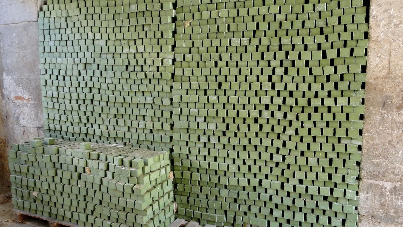 Hunderte gestapelte grüne Seifenstücke trocknen in hohen, luftigen Stapeln an einer Steinwand.