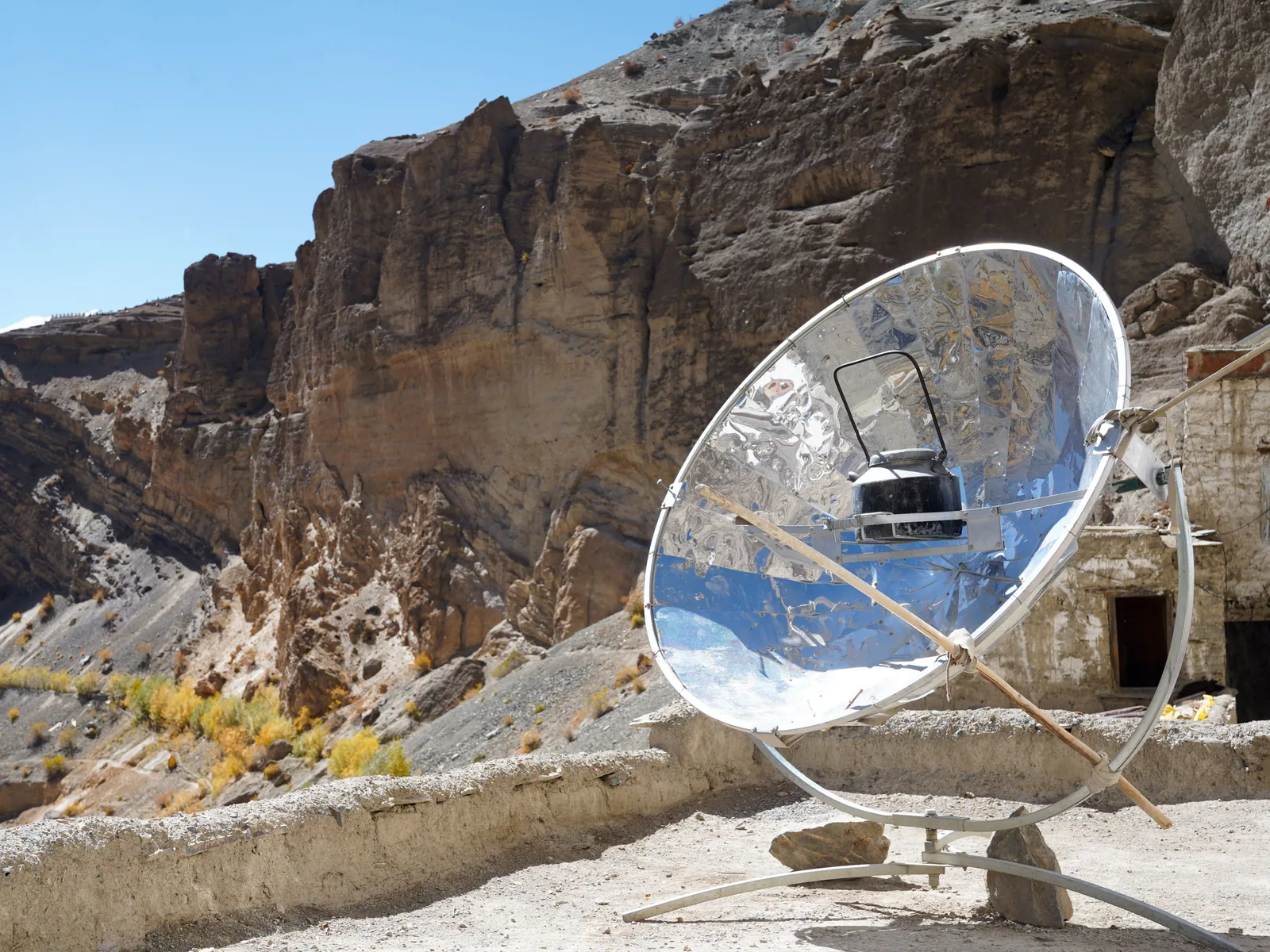 Ein runder Parabolspiegel aus spiegelnden Segmenten auf einem Metallgestell, im Brennpunkt ein dunkler Kessel, im Hintergrund Felswände im Hochgebirge.