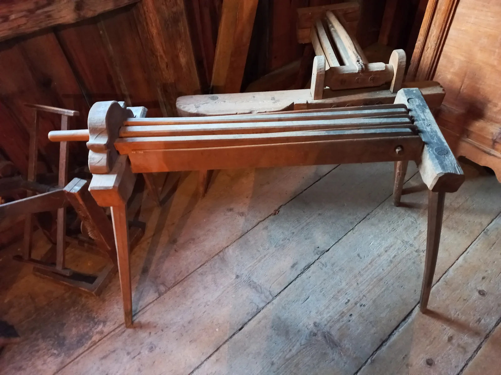 Eine hölzerne Flachsbreche mit schwenkbarem Oberteil und Leisten im Unterteil steht auf einem Holzboden in einem Museum.