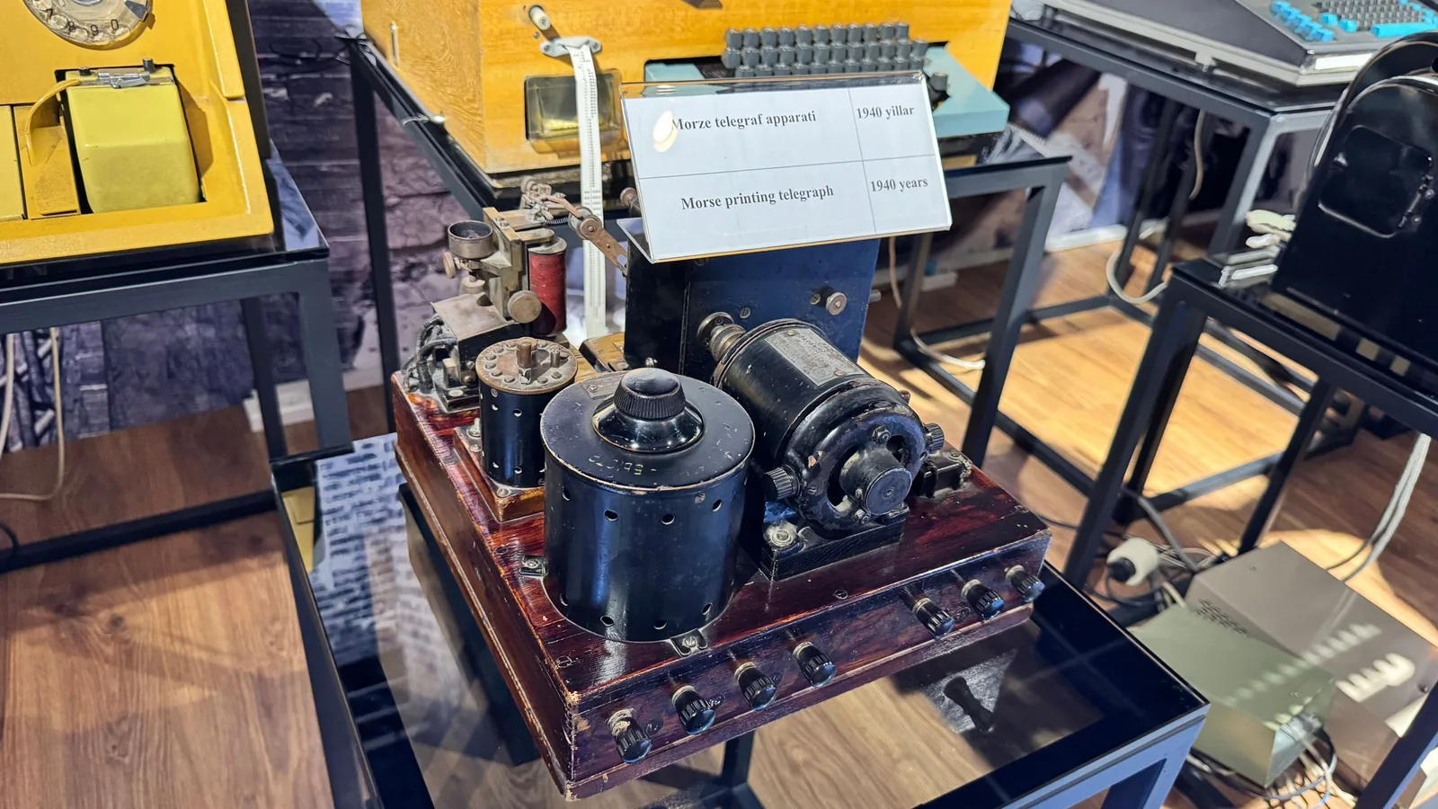 Ein historisches Morse-Telegrafengerät mit Taster, Schreibmechanik und Metallgestell steht in einer Ausstellung.