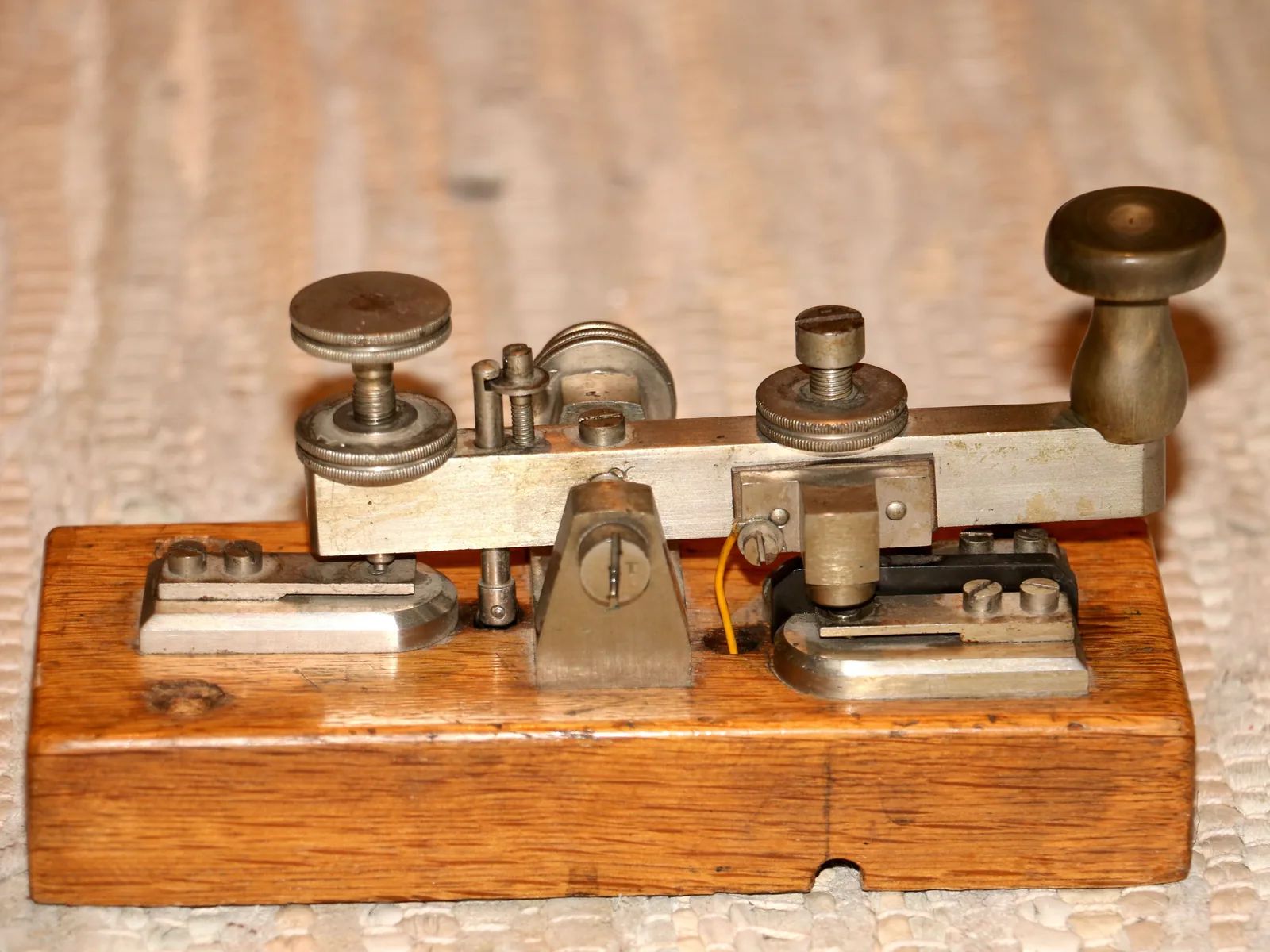 Eine alte Morsetaste aus Messing mit schwarzem Drehknopf auf einem Holzsockel, von der Seite fotografiert.
