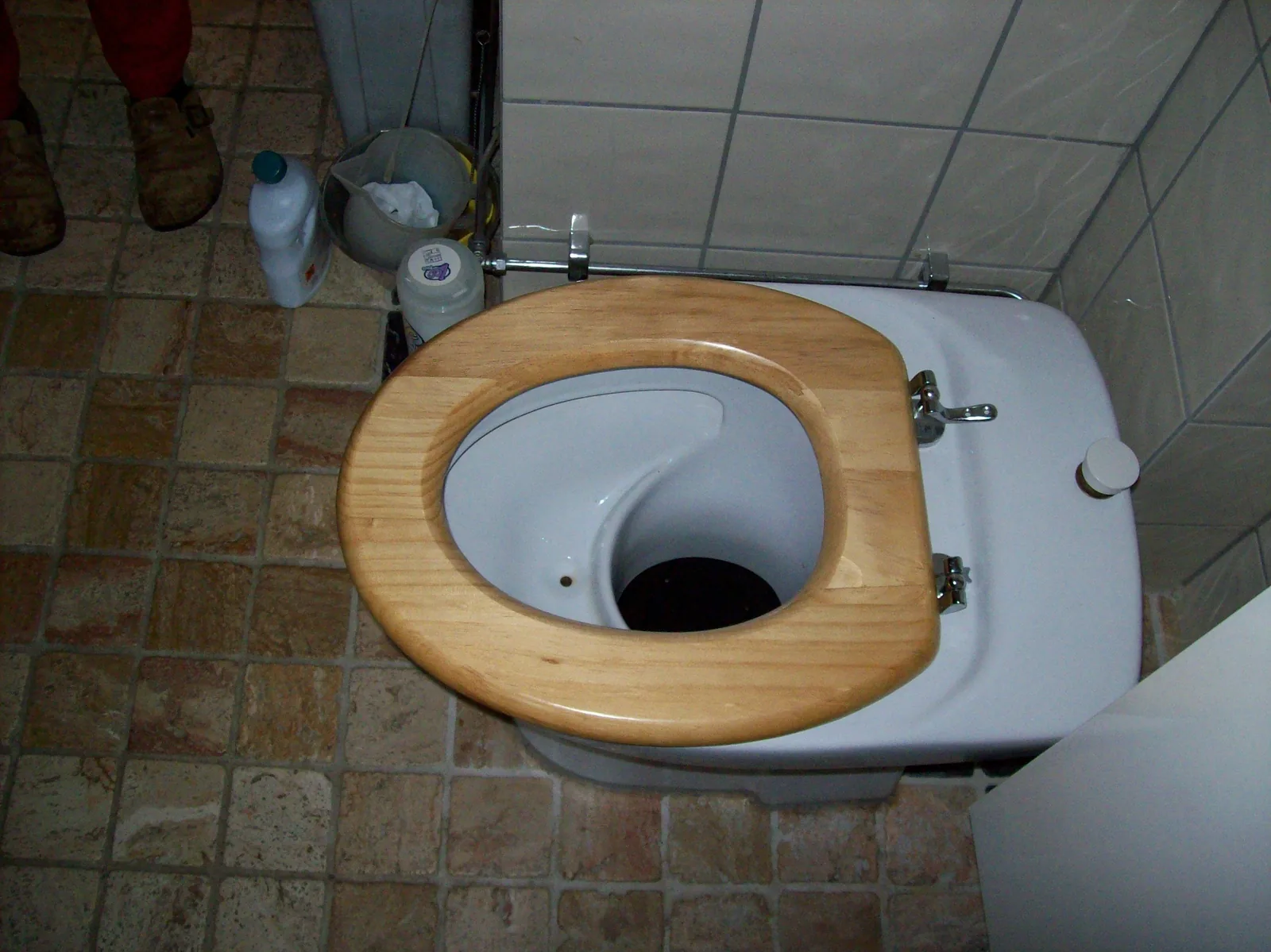 Blick von oben auf eine Trenntoilette mit Holzsitz in einem gefliesten Bad: vorne eine flache Mulde, die den Urin auffängt, dahinter die Öffnung für die Feststoffe.