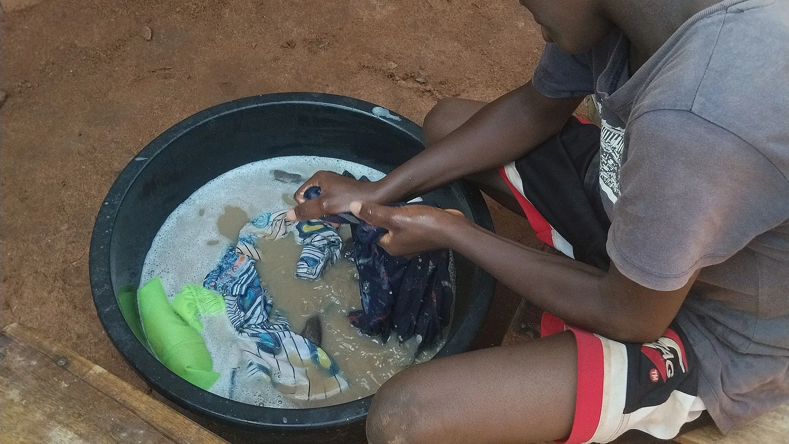 Ein Junge wäscht Kleidung von Hand in einer mit Seifenwasser gefüllten Schüssel.