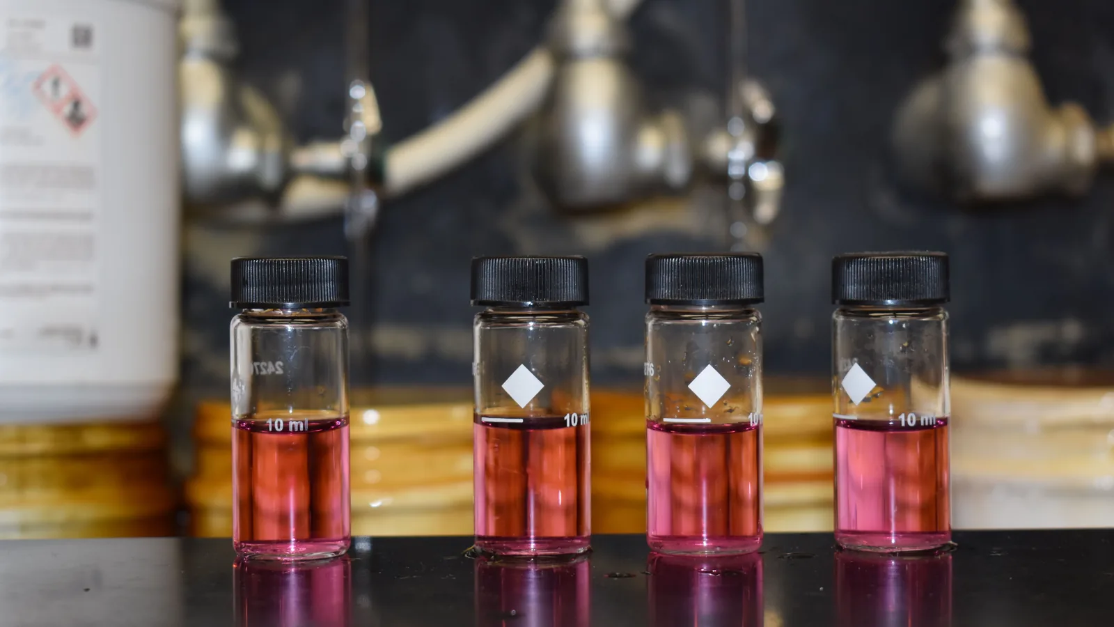 Vier kleine Probengläser mit Trinkwasser stehen nebeneinander; das Wasser darin hat sich nach Zugabe eines Testreagenzes rosa bis rot gefärbt.