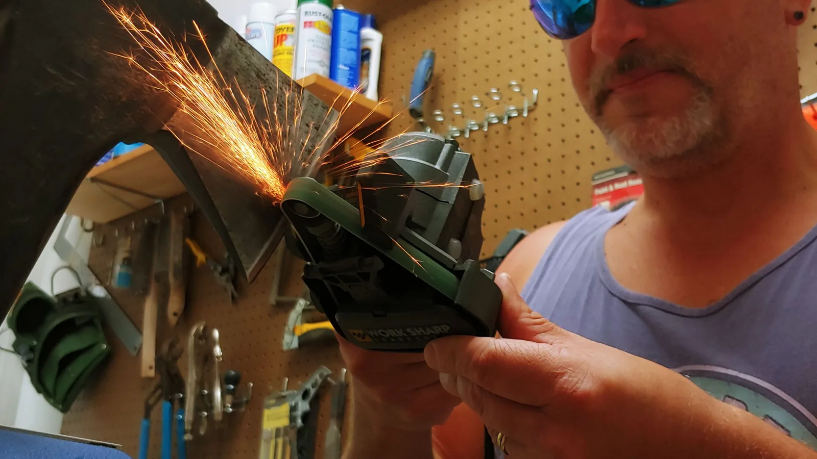 Eine Axt wird in einem Schraubstock fixiert und mit einem Bandschleifer geschärft.