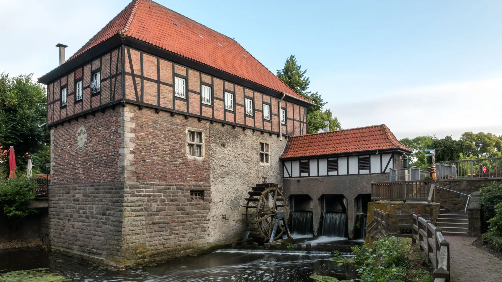 Die Borgmühle in Lüdinghausen: ein Fachwerkbau auf massivem Steinsockel am Wasser, daneben ein Wasserrad und das Wehr, über das der Bach abfließt.