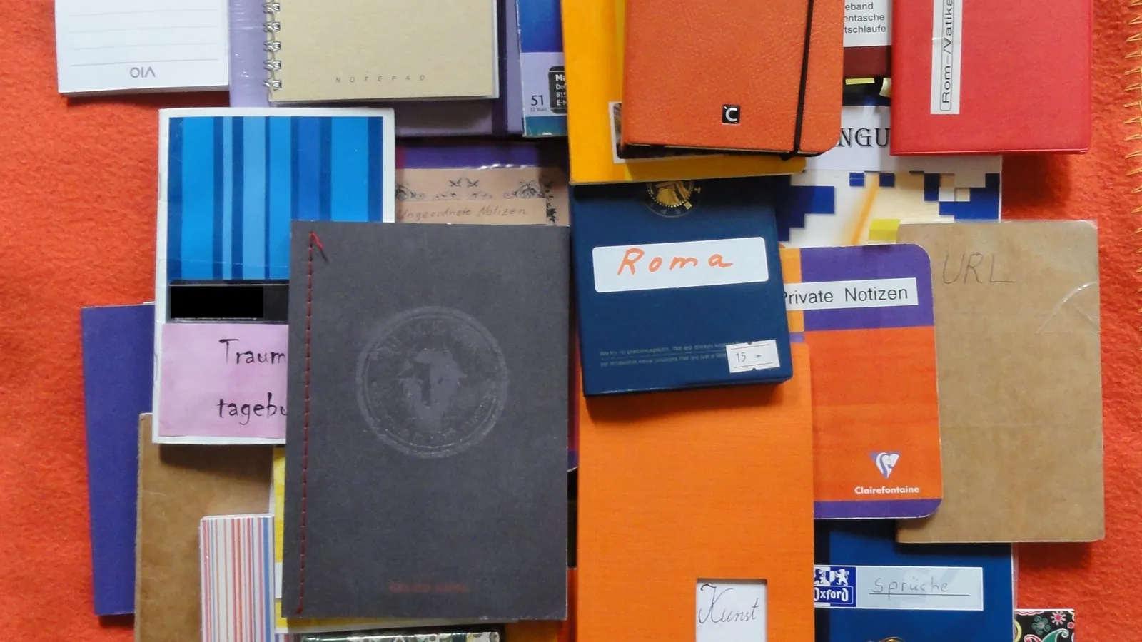 Mehrere Notizbücher und Schreibblöcke liegen übereinander auf einer Fläche.