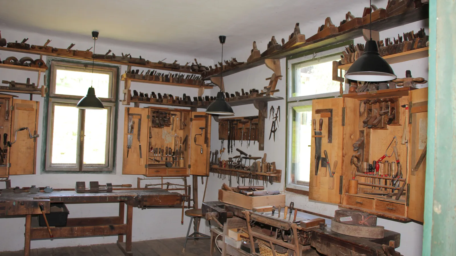 Alte Tischlerwerkstatt im Freilichtmuseum: zwei Hobelbänke, an den Wänden offene Werkzeugschränke mit Sägen und Zwingen, darüber Regale voller Hobel.