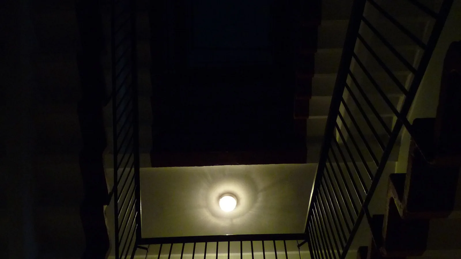 Ein dunkles Treppenhaus in einem Mehrfamilienhaus führt über mehrere Etagen nach oben.